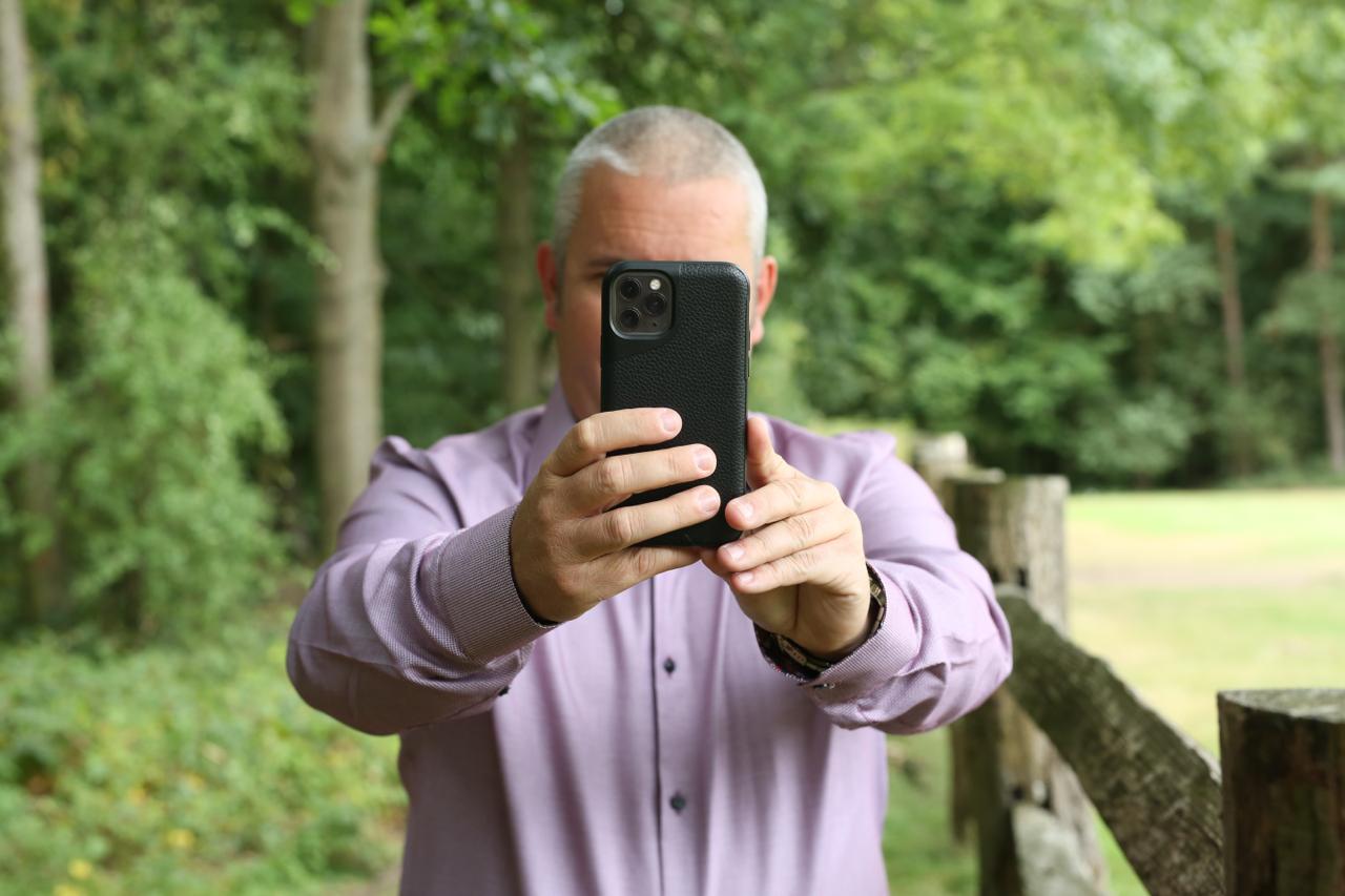 Brett Sheldon taking a photograph on his phone in the woodland